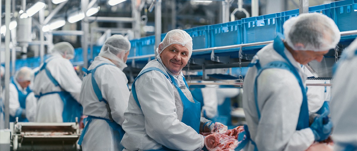 Ein Mitarbeiter schneidet ein Stück Fleisch.