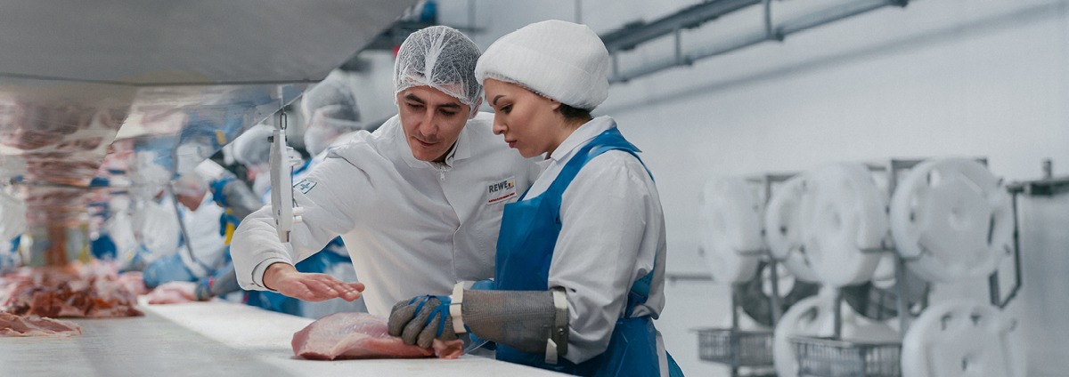 Ein Mitarbeiter schneidet ein Stück Fleisch.